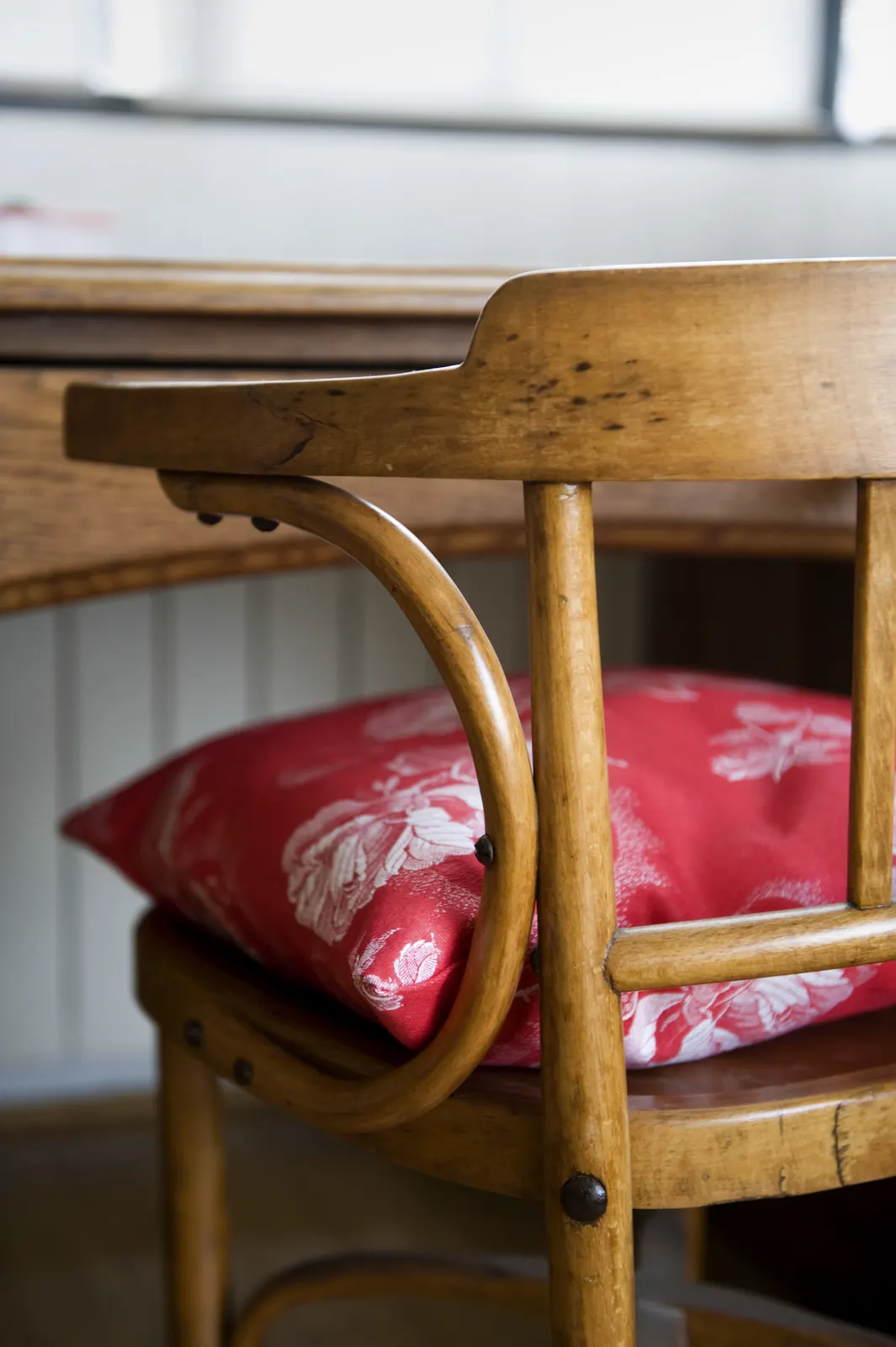 A bentwood chair at a wooden desk with a red floral cushion